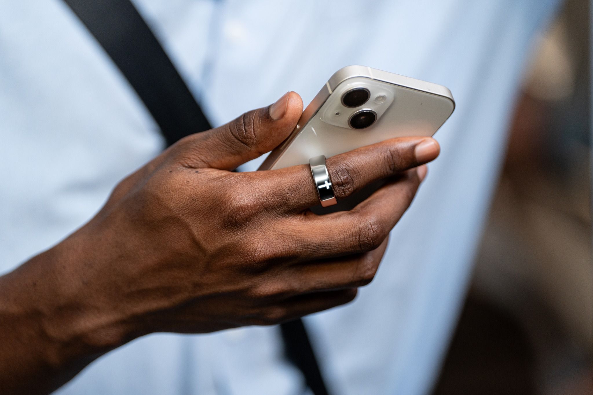 A hand wearing Elah Ring while holding a phone, with the Cross Light visible.